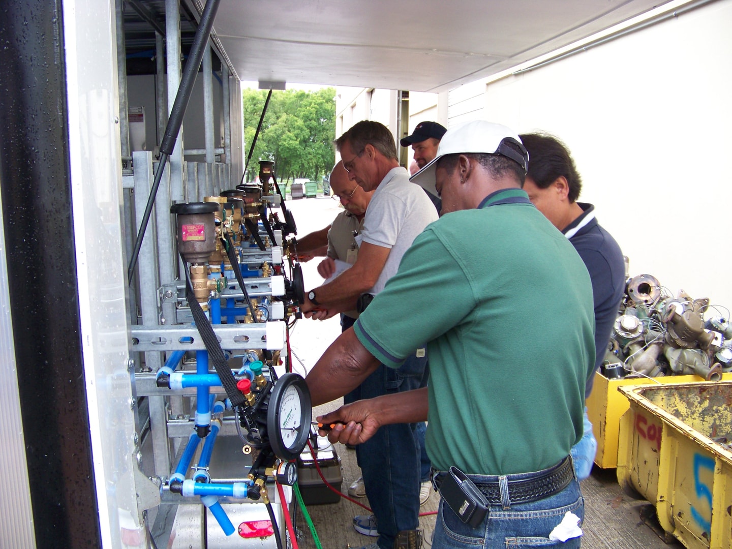 Workers examining blue piping backflow assembly panel